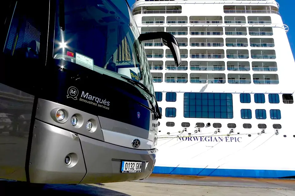 Autocar Beulas VIP de la flota Marqués junto a un barco en el puerto.